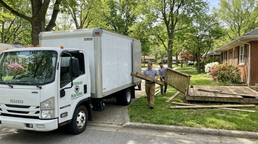 Veteran Hauling white Isuzu box truck parked in front of a Carmel-style Central Indiana suburban brick ranch home with a partially torn-down wood deck and crew loading=